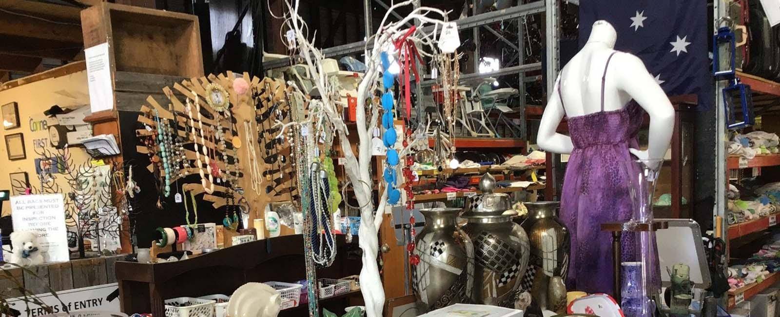 Photo from inside Op Shop with an assortment of second hand items - a purple dress on a mannequin, jewellery hanging on a stand and other bits and pieces. 