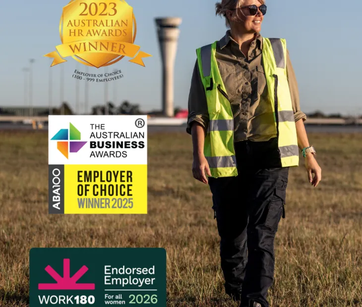 An airside operations officer walking with the air traffic control tower in the background.