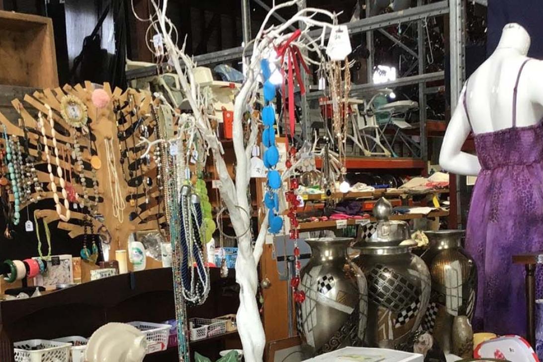 Photo from inside Op Shop with an assortment of second hand items - a purple dress on a mannequin, jewellery hanging on a stand and other bits and pieces. 