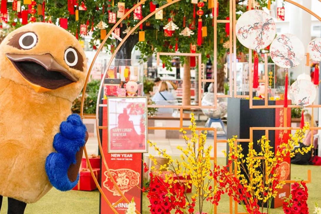 A person dressed in a kookaburra costume next to lunar new year decorations