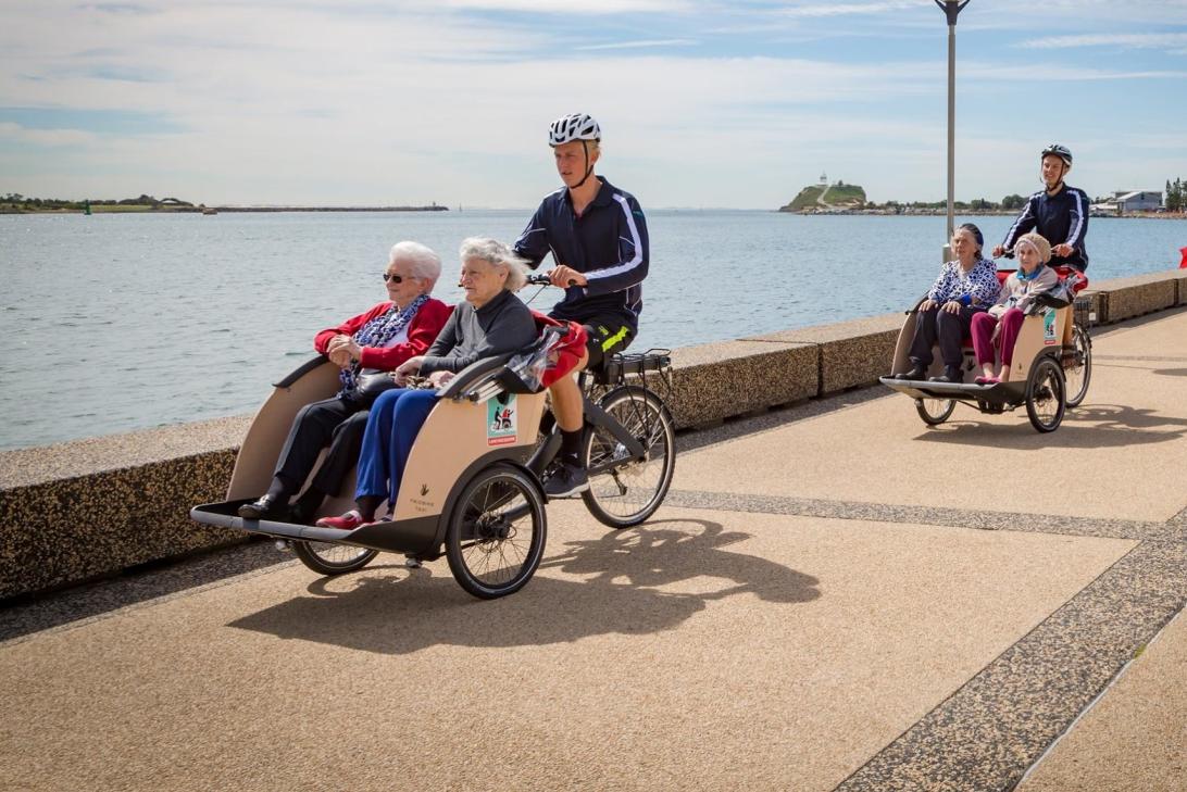 two cyclists with elderly passengers cycling along a path near water