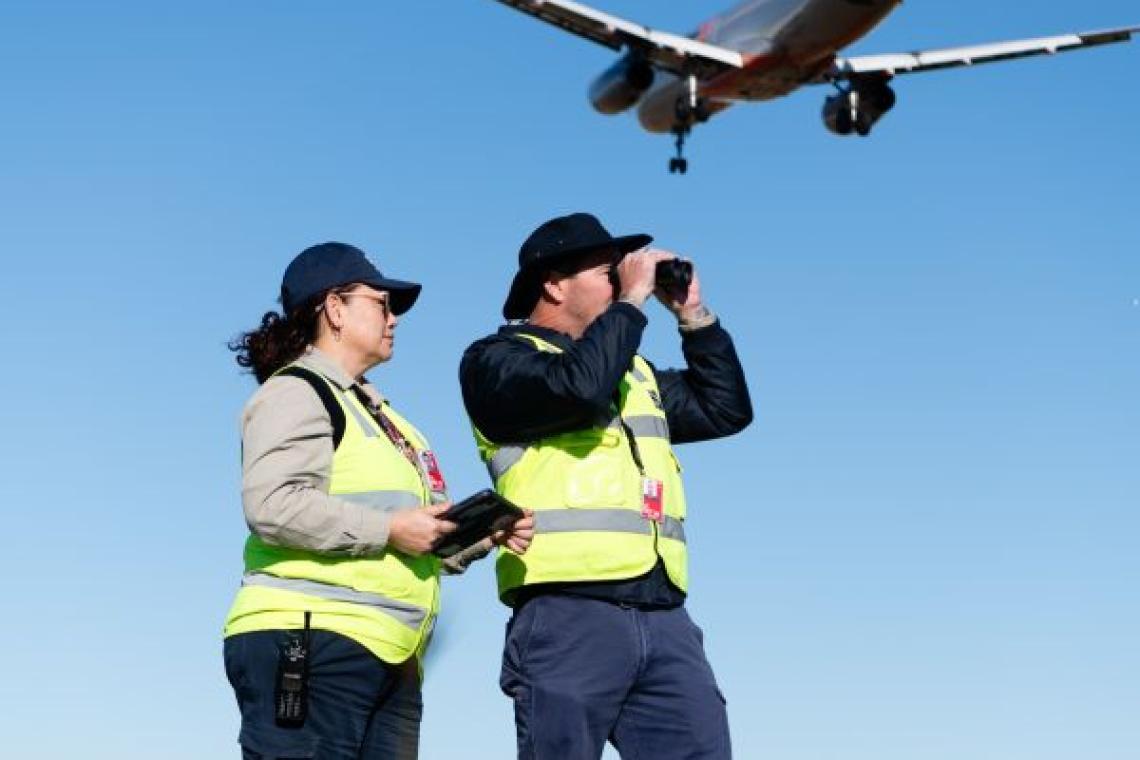 Two airside officers with a Jetstar plane flying overhead
